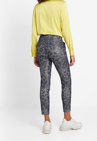 Navy-siniset housut valkoisella kukkakuviolla, slim fit, korkea vyötärö, yhdistetty keltaiseen paitaan ja valkoisiin tennareihin. Sujuva pinta, kapeneva lahje.