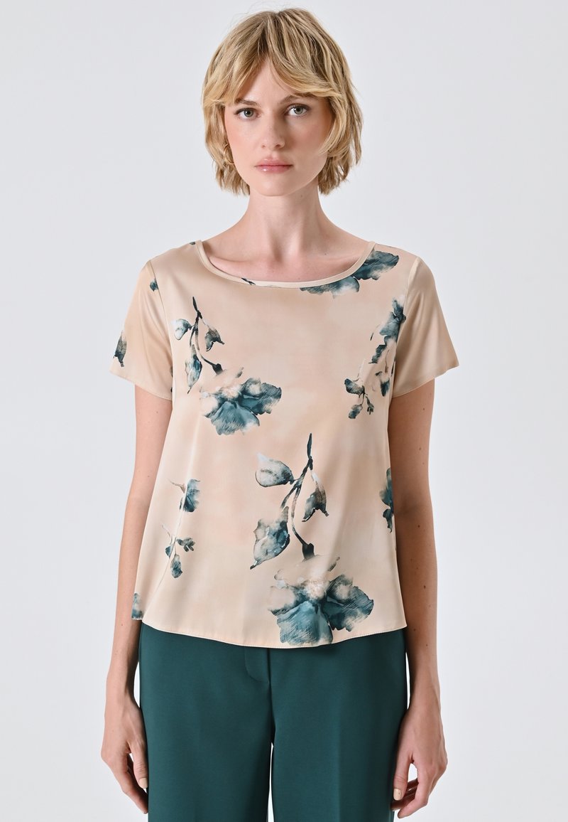 Blusa a stampa floreale in beige chiaro con accentuazioni blu-verdi, maniche corte e scollo rotondo. Tessuto leggero e liscio con una vestibilità rilassata.