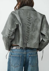 Ingekorte grijze leren jas met veterdetails langs de mouwen en achterkant. Draag het over hoge spijkerbroek met een paillettenriem.