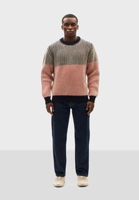 Textured sweater in navy, beige, and pink stripes with a ribbed design; worn with dark pants and light sneakers. Medium-fit, crew neck style.