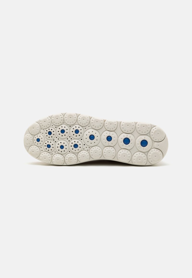 Suela de zapato de goma blanca con patrones circulares y ovalados, con pequeños acentos azules. Superficie texturizada con orificios de ventilación en toda su extensión.