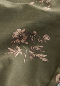  Oliivinvihreä kukkakuvioinen kangas. Siinä on beigejä kukkia ja lehtiä. Sileä pinta, jossa on kevyt kiilto, taiteltu näyttämään syvyyttä.