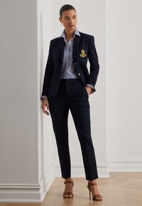 Tamsiai mėlynas pritaikytas švarkas su auksiniu siuvinėjimu, derinamas su dryžuota marškinių apykakle ir siaurėjančiomis tamsiai mėlynomis kelnėmis. Šviesiai rudi aukštakulniai sandalai.