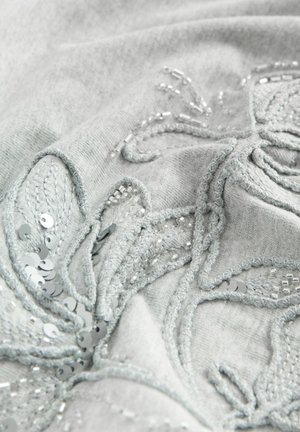 Grauer Stoff mit detaillierter Blumenstickerei, verziert mit silbernen Pailletten und Perlen. Die Textur ist weich und hat erhabene Stickakzente.