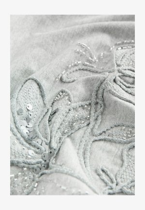 Tessuto grigio con ricami floreali dettagliati, arricchito da paillettes argento e perline. La texture è morbida con accenti di cuciture in rilievo.