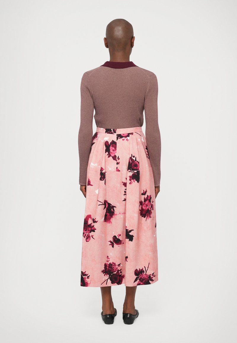 Ribbad mauvröd tröja med krämfärgad krage i maroon, tillsammans med en rosa blommönstrad kjol med stora mörka rosor och en utställd siluett.