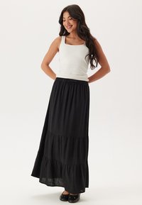 Zwarte maxi rok gemaakt van lichtgewicht stof met een gelaagde ontwerp en een elastische tailleband. Gecombineerd met een aansluitend wit tanktop.