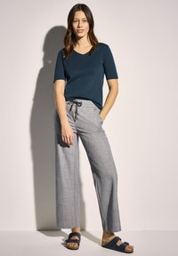 Námořnické tričko s výstřihem do V a krátkým rukávem spárované se světle šedými širokými kalhotami s šňůrkou v pase. V kombinaci s tmavě modrými sandály.