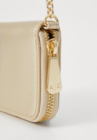 Elegante portafoglio beige con cerniera e hardware dorato, caratterizzato da una superficie testurizzata e un logo ben visibile sulla zip.