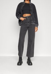 Veste noire courte avec une fermeture éclair à l'avant, associée à un jean noir taille haute à jambes larges et des bottines noires épaisses. Texture lisse.