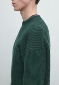 Dunkelgrüner, gerippter Strickpullover mit rundem Ausschnitt und strukturiertem Muster. Die Ärmel haben ein leicht überschnittenes Schulterdesign.