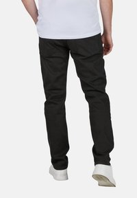 Vaqueros de mezclilla negra con corte ajustado, con bolsillos traseros y costuras mínimas. Combinados con zapatillas blancas para crear contraste.