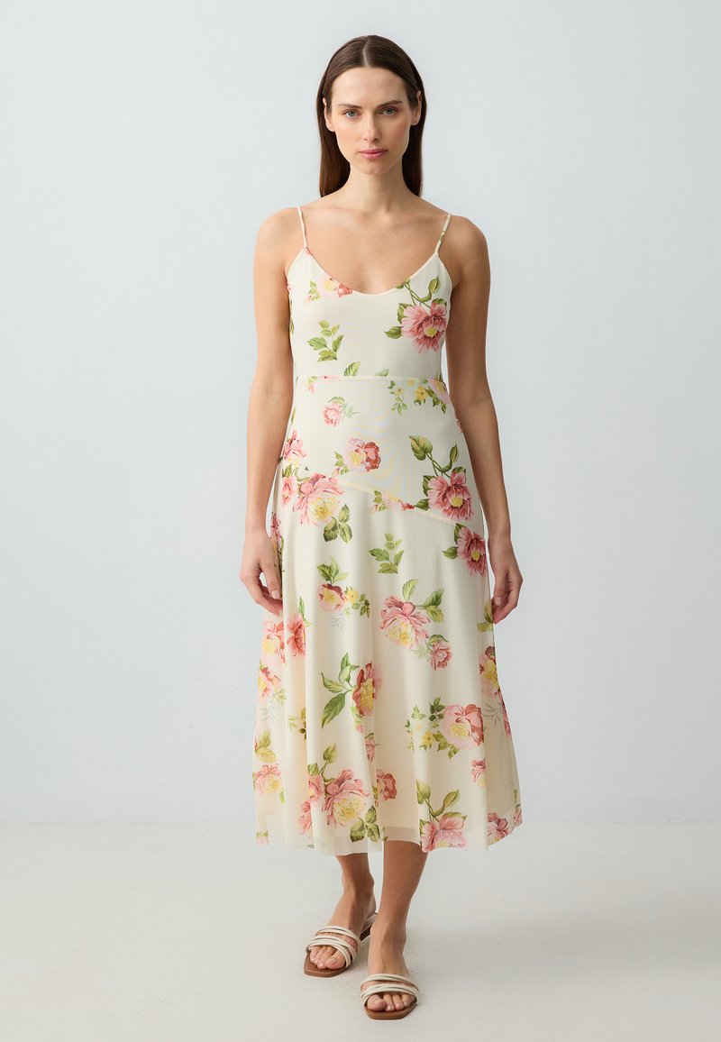 Robe midi florale avec bretelles fines, présentant un fond crème clair orné de pivoines roses et de feuilles vertes. Tissu lisse et fluide.