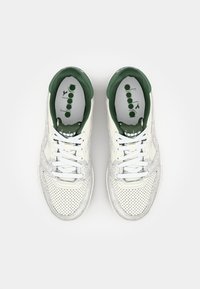 White sneakers with green accents, featuring a perforated design, rounded toe, and white laces; branding visible on the insoles.