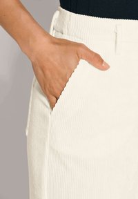 Witte ribfluwelen rok met textuur en een zijzak, met een hand die in de zak is geplaatst voor schaling.