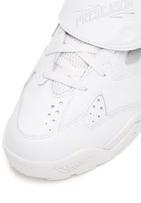 Biały sneaker z gładką skórzaną cholewką, siateczkowymi wstawkami, perforowanymi detalami, grubą białą gumową podeszwą oraz regulowanym paskiem z wytłoczonym logo.