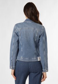 Giacca in denim di colore azzurro chiaro, con maniche lunghe, polsini con bottone e un taglio dritto con cuciture posteriori. Include un'etichetta con il logo in vita.