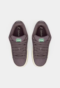 Tamno ljubičaste tenisice s glatkim tekstilnim gornjištem, ravnim vezicama, bijelim gumenim potplatom i zelenim Puma logotipom na jeziku. Vidljiva Ortholite® uložak.