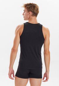 Black sleeveless tank top made of soft fabric, featuring a fitted design and smooth texture, layered over matching shorts.