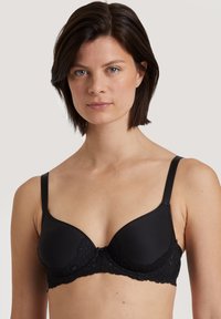 Zwarte beha met gladde, gewatteerde cups en ingewikkelde kanten details bij de band. Verstelbare banden en een haak- en oogsluiting aan de achterkant.