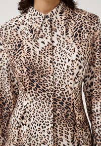 Blúzka s leopardím vzorom, ktorá má vysoký golier, zapínanie na gombíky a hladký, ľahký materiál v kombinácii béžových a čiernych odtieňov.