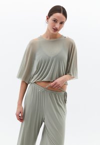 Ljusgrön, genomskinlig kort topp med vida ärmar, kombinerad med matchande vida byxor med elastisk midja och dragsko.