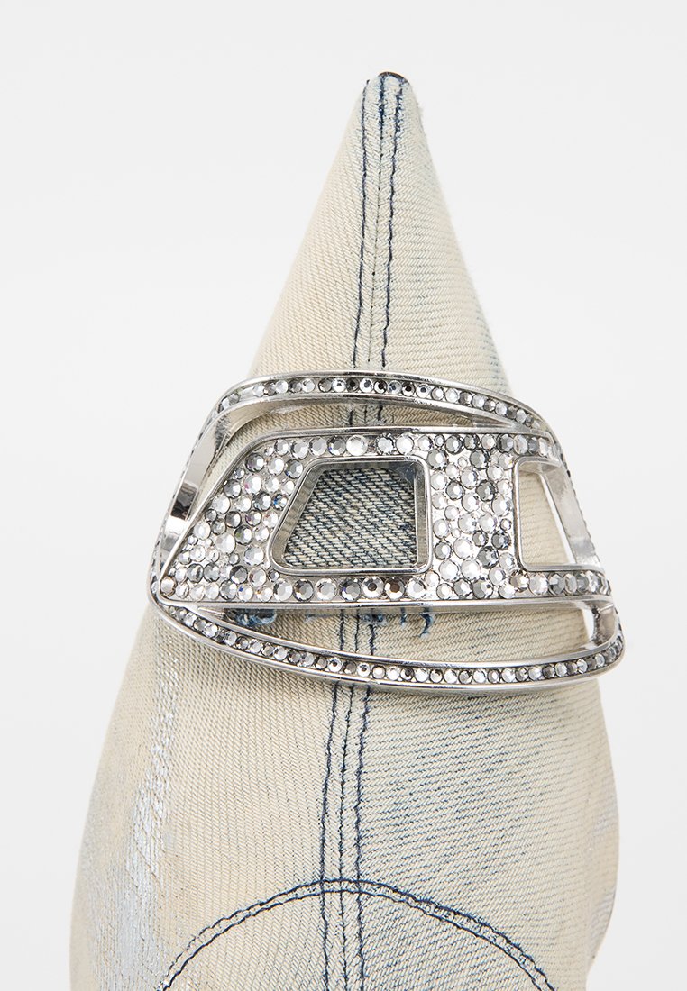 Fibbia decorativa argento con un design geometrico, decorata con cristalli trasparenti, posta su uno sfondo in tessuto crema textures.