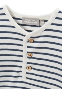 Chemise pour bébé blanche et marine à rayures avec trois boutons en bois et une étiquette indiquant la taille 6 mois.