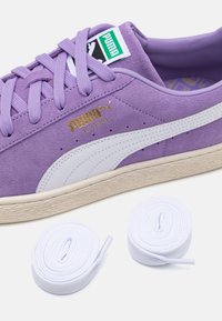 Fioletowe zamszowe sneakersy z białymi akcentami i teksturowaną gumową podeszwą. W zestawie dwa białe sznurówki zwinięte obok buta. Złoty detal z logo.