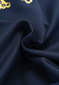 Navy blue fabric with a smooth texture, featuring golden accents in a floral pattern, draped to show its pliable qualities and structure.