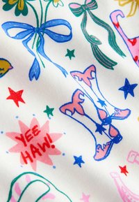 Tissu blanc avec des illustrations colorées de bottes, nœuds, étoiles et fleurs, accompagné d'un texte rouge "YEE HAW !" dans un design ludique.