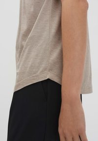Camicia beige a maniche corte con finitura testurizzata, caratterizzata da un orlo curvo e spacco laterale, abbinata a pantaloni neri.