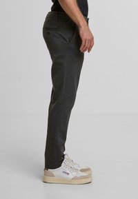 Pantalon gris à coupe slim, avec des poches latérales et une poche arrière, associé à des baskets blanches et beige. Texture de tissu lisse.