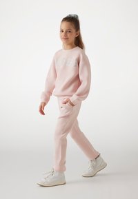 Sudadera rosa y joggers a juego con un logo metálico. El conjunto se complementa con zapatillas altas blancas para un look casual.