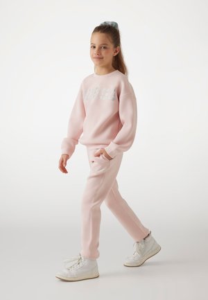 Felpa rosa e joggers abbinati con un logo metallico. L'outfit è completato da sneakers bianche alte per un look casual.