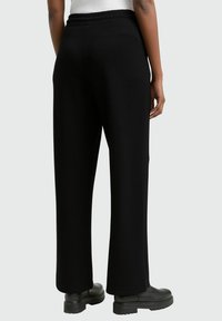 Schwarze weit geschnittene Hose mit elastischem Bund, ausgestattet mit einer glatten Textur und einem lockeren Schnitt. Tragen mit schwarzen klobigen Stiefeln.