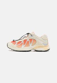 Chaussure de sport Salomon avec un dessus beige, des accents en mesh orange, des superpositions grises, un système de maintien des lacets et une semelle extérieure texturée noire.