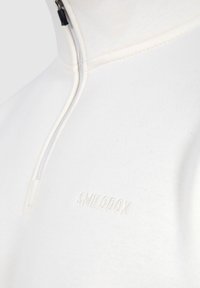 Witte quarter-zip pullover van zachte stof, met een subtiele reliëflogo en contrasterende ritsdetails. Gladde textuur, slim fit ontwerp.