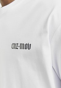 Hvid bomulds t-shirt med sort tekst "cnz-mov" i en fed, stiliseret skrifttype på venstre brystområde. Glat tekstur, klassisk crew neck.