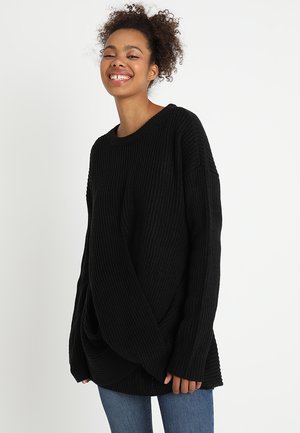 Black knit sweater with a loose fit, ribbed texture, wide neckline, and dropped shoulders, paired with blue jeans.