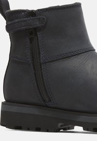 Botín de cuero navy con tobillo que presenta una cremallera lateral, costuras en contraste y una resistente suela de goma negra con un agarre texturizado.