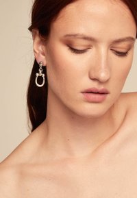 Orecchini a cerchio in argento con un design circolare, caratterizzati da un link a catena e accenti sferici, esposti su un modello con uno sfondo neutro.