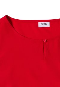 Rote Bluse mit rundem Ausschnitt, die an der Vorderseite über ein kleines Knopfdetail verfügt. Hergestellt aus glattem Stoff mit leichtem Griff.
