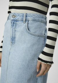 Light blue denim skirt with a high waist, front pockets, and visible stitching. Paired with a black and white striped ribbed top.