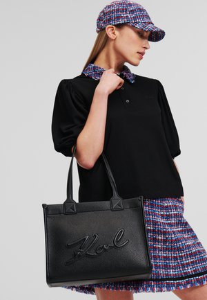 Black leather tote bag with embossed “Karl” logo, featuring structured shape, durable handles, and subtle textured finish.