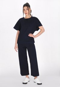 Námořnický modrý texturovaný dámský dvoudílný outfit se zkráceným rukávem a širokými kalhotami, doplněný o bílé tenisky.