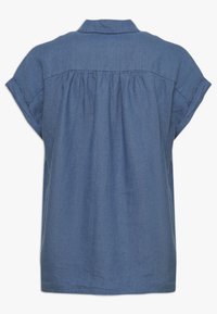 Jeansskjorta med krage, korta uppvikta ärmar och en rynkad bakdel. Har en enfärgad blå färg och lättviktsmaterial.