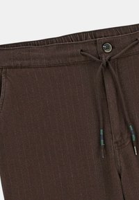 Pantalons marron à taille élastique avec cordon de serrage ajustable, présentant de fines rayures verticales et un détail de bouton à la taille.