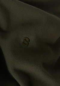 Tecido verde oliva con una superficie suave y texturizada que presenta una pequeña "S" bordada en un color de hilo a juego.