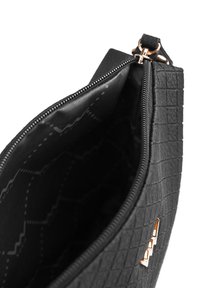 Detailní záběr na černou texturovanou kabelku se zlatým zipem a sponou, zobrazující částečně otevřenou horní část a vzorované látkové vnitřní podšívku.